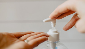 A close up photo of someone's hands as they use an anti-bacterial hand gel dispenser