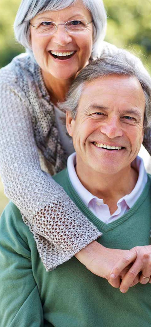 A photo showing an older couple smiling in the sunshine